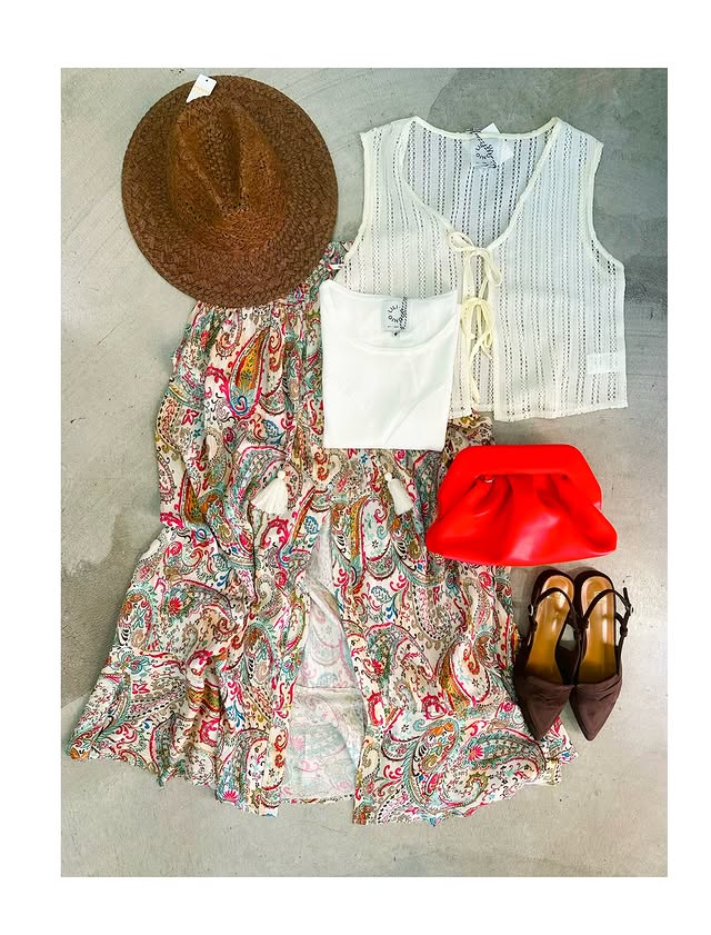 Gonna lunga con stampa paisley multicolore su fondo bianco panna, fotografata distesa insieme a cappello in paglia, top bianco, gilet in maglia, pochette rossa e décolleté