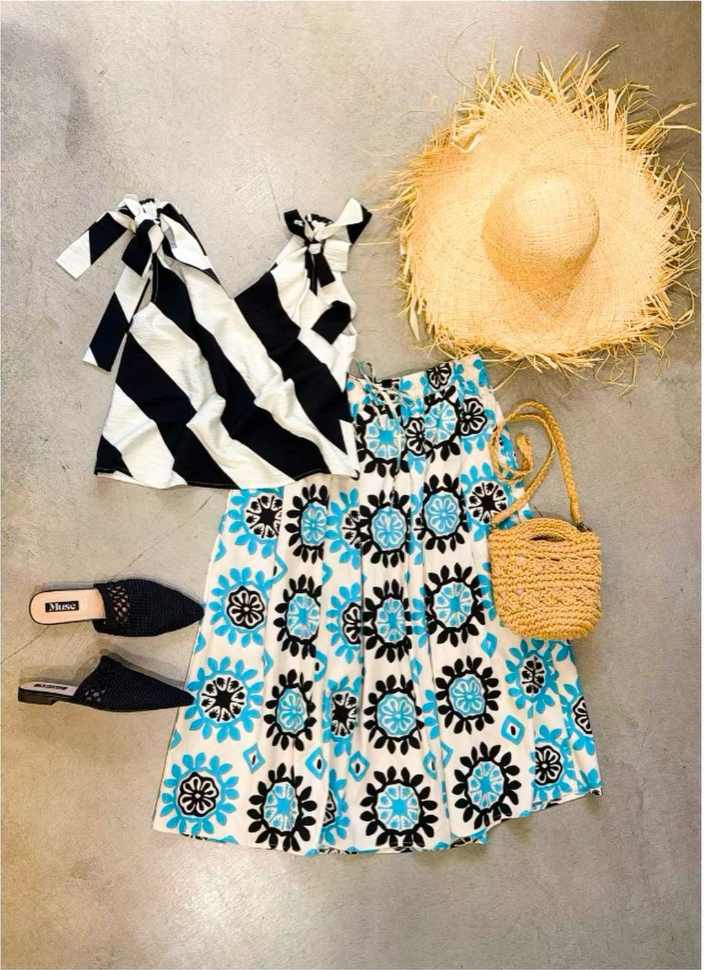 Gonna midi in popeline bianco con medaglioni turchese e nero distesa, abbinata a un top a righe bianche e nere, cappello di rafia, borsa crochet e mules nere